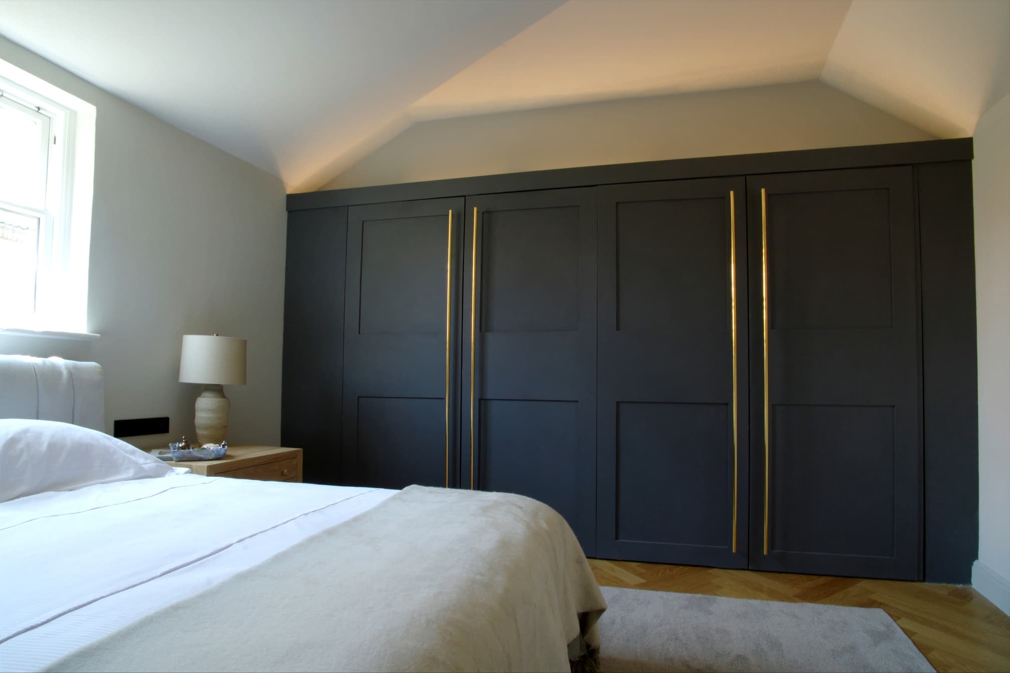Charcoal shaker fitted wardrobes built up to and scribed around a sloping ceiling, with long brass bar handles