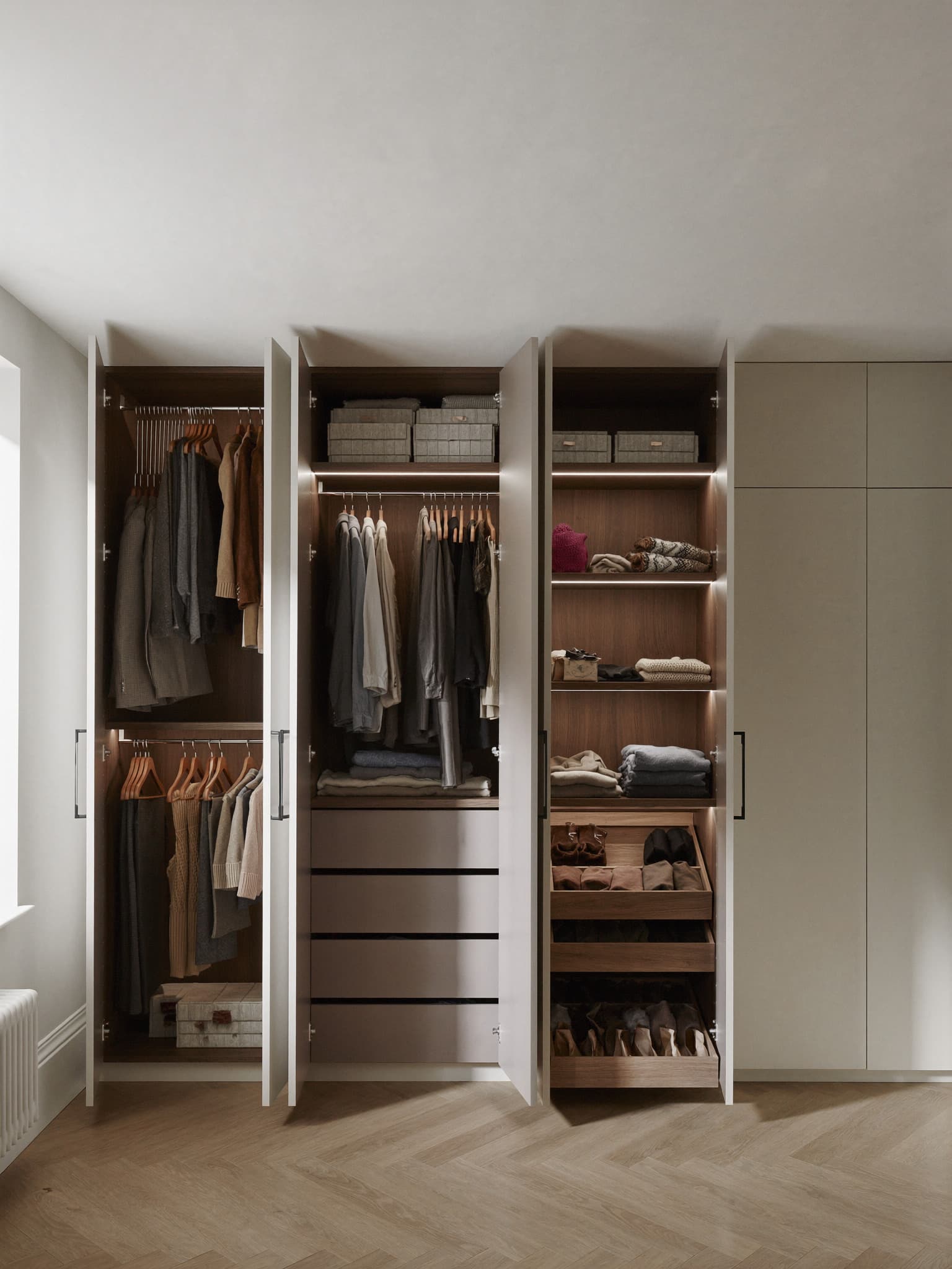 Fitted wardrobes with the doors open, showing walnut-lined interiors, lit shelving, hanging rails, drawers and pull-out shoe storage