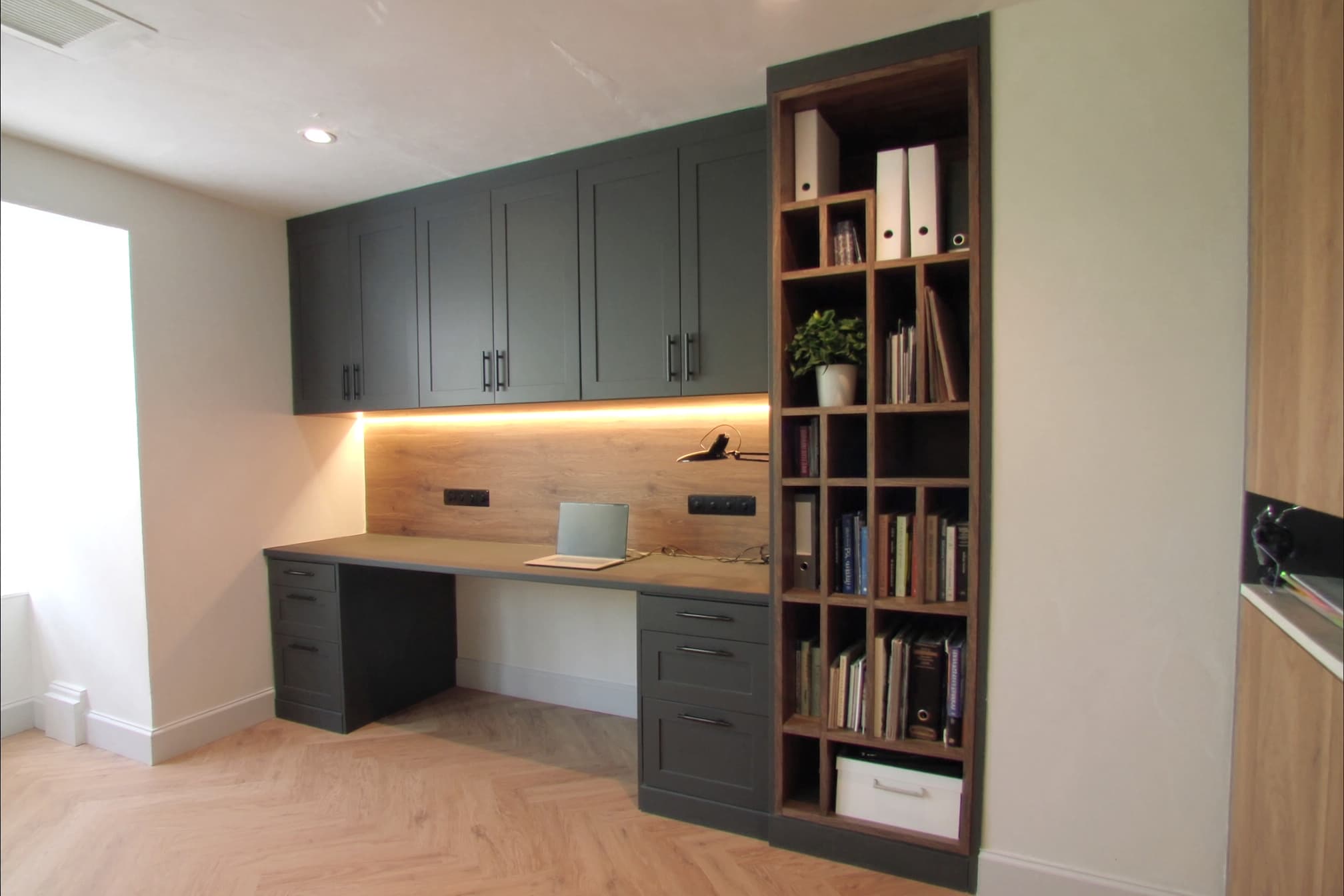 A fitted home office in graphite shaker with a warm oak back panel, lit shelving and a herringbone floor